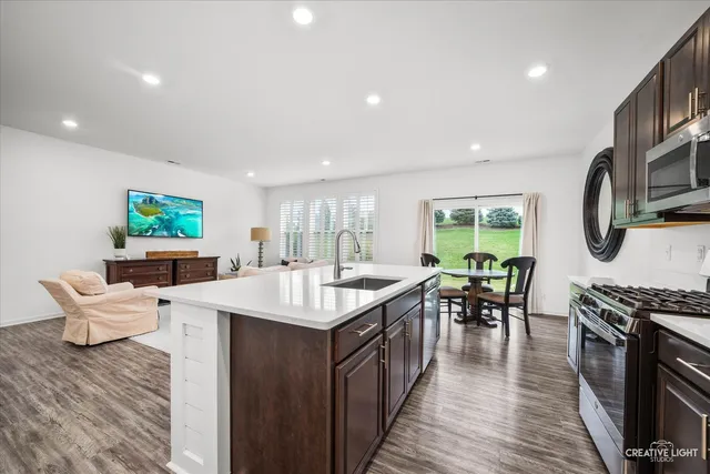 a living room with stainless steel appliances furniture a rug and a kitchen view