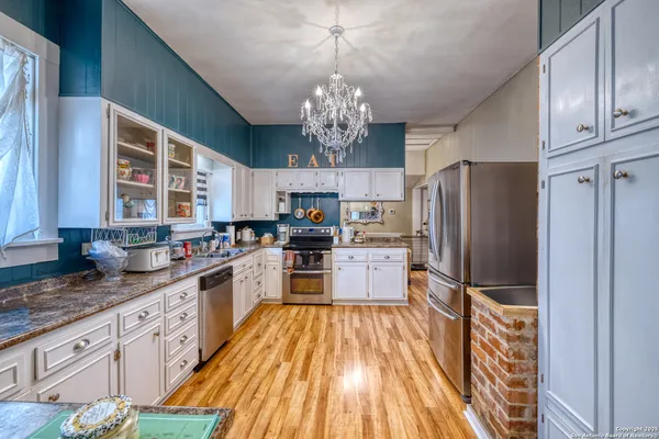 a kitchen with granite countertop stainless steel appliances a refrigerator oven a sink dishwasher and white cabinets with wooden floor