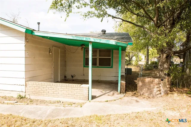 a view of yellow house with a large tree and wooden fence