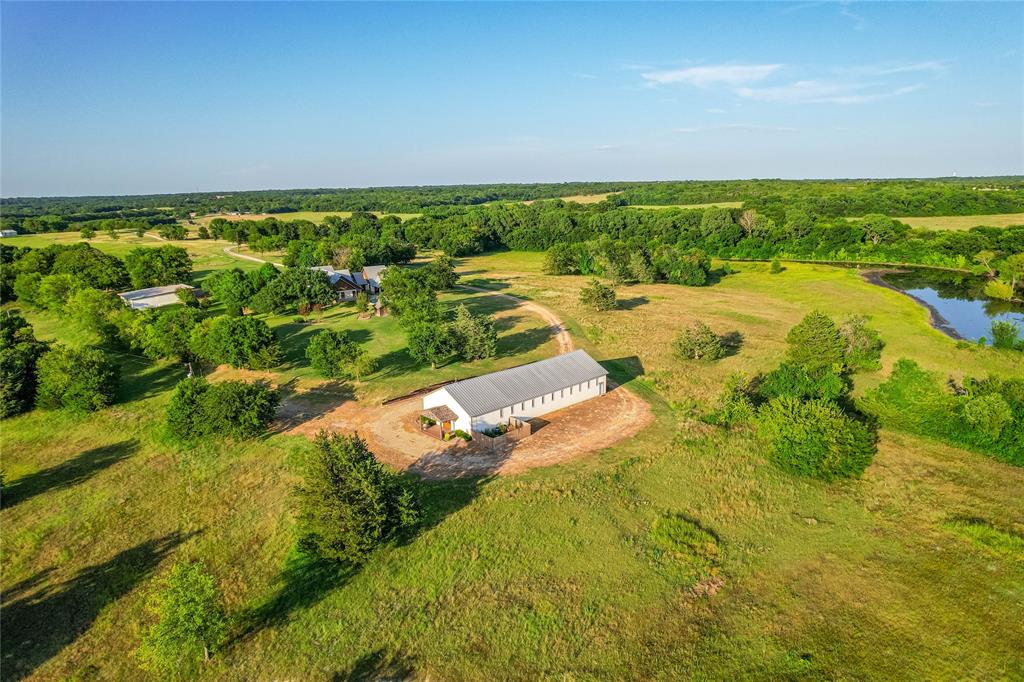 1922 A Bethel-Cannon Road Whitewright, TX 75491 - Photo 38 of 40 Expansive rural property featuring a large outbuilding with multiple windows, a winding dirt road, scattered mature trees, and a natural pond