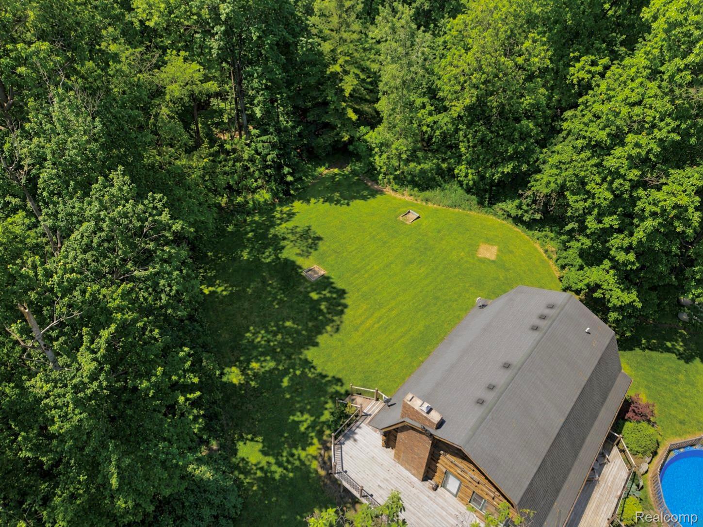 14830 Sheridan Road Byron, MI 48418 - Photo 73 of 74 Rear exterior featuring a multi-level wood deck, a circular above-ground pool, and a large grassy area surrounded by mature trees