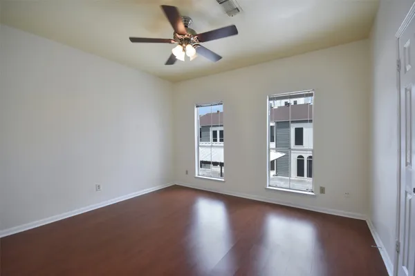 an empty room with wooden floor chandelier fan and windows