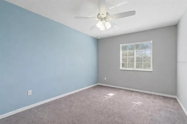 an empty room with a chandelier fan and windows