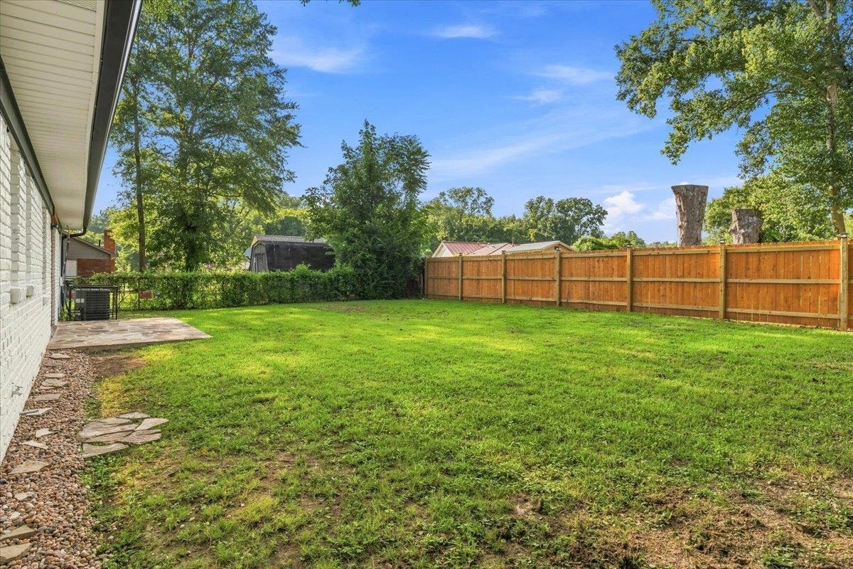 1744 West Holmes Road Memphis, TN 38109 - Photo 18 of 24 Expansive green lawn, wood fence perimeter, concrete patio, white brick exterior, mature trees