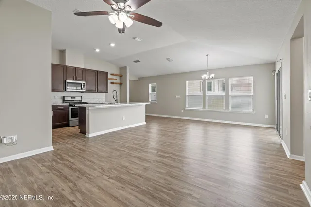 an empty room with wooden floor kitchen view and a window