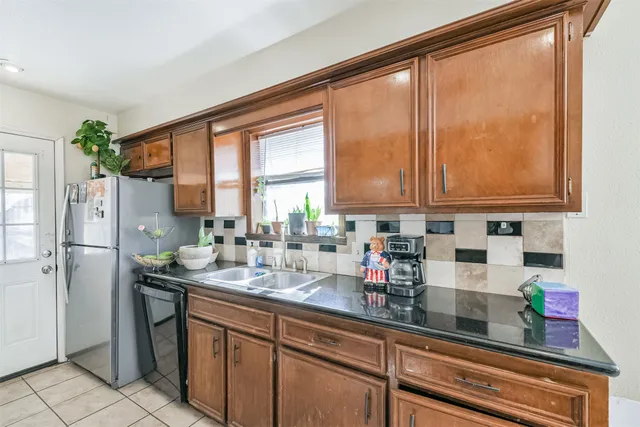 a kitchen with stainless steel appliances granite countertop a refrigerator a sink and white cabinets next to a window