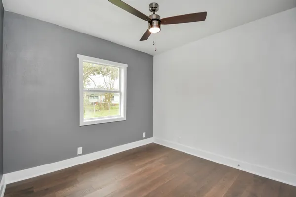 an empty room with wooden floor ceiling fan and windows