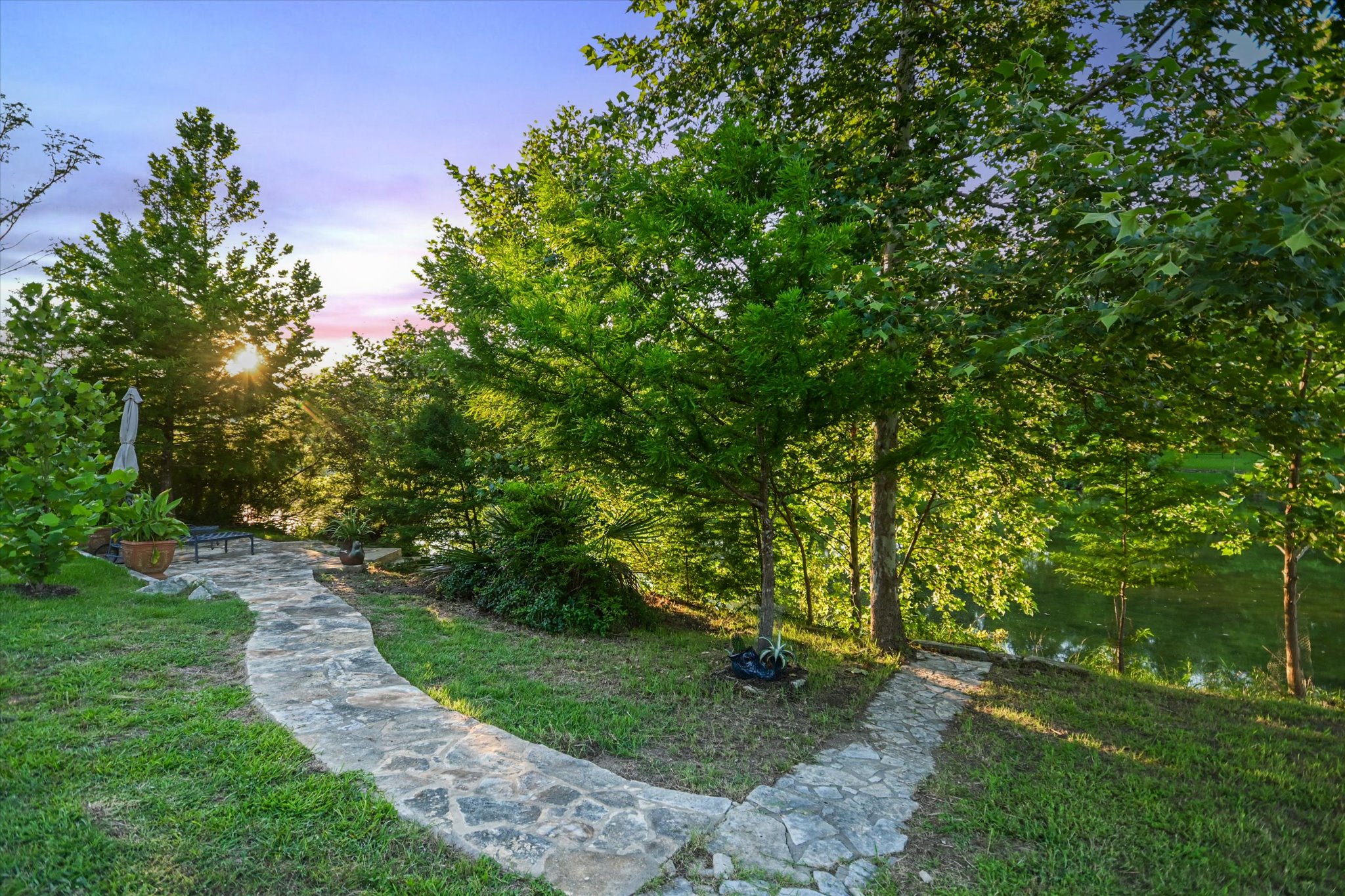 2411 Spoke Hollow Road Wimberley, TX 78676 - Photo 27 of 37 Meandering stone pathway leads to a tranquil, naturally illuminated lakefront setting.