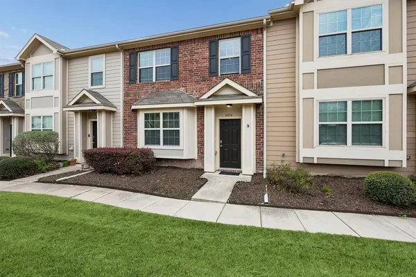 a view of a brick house with a yard plants and large tree