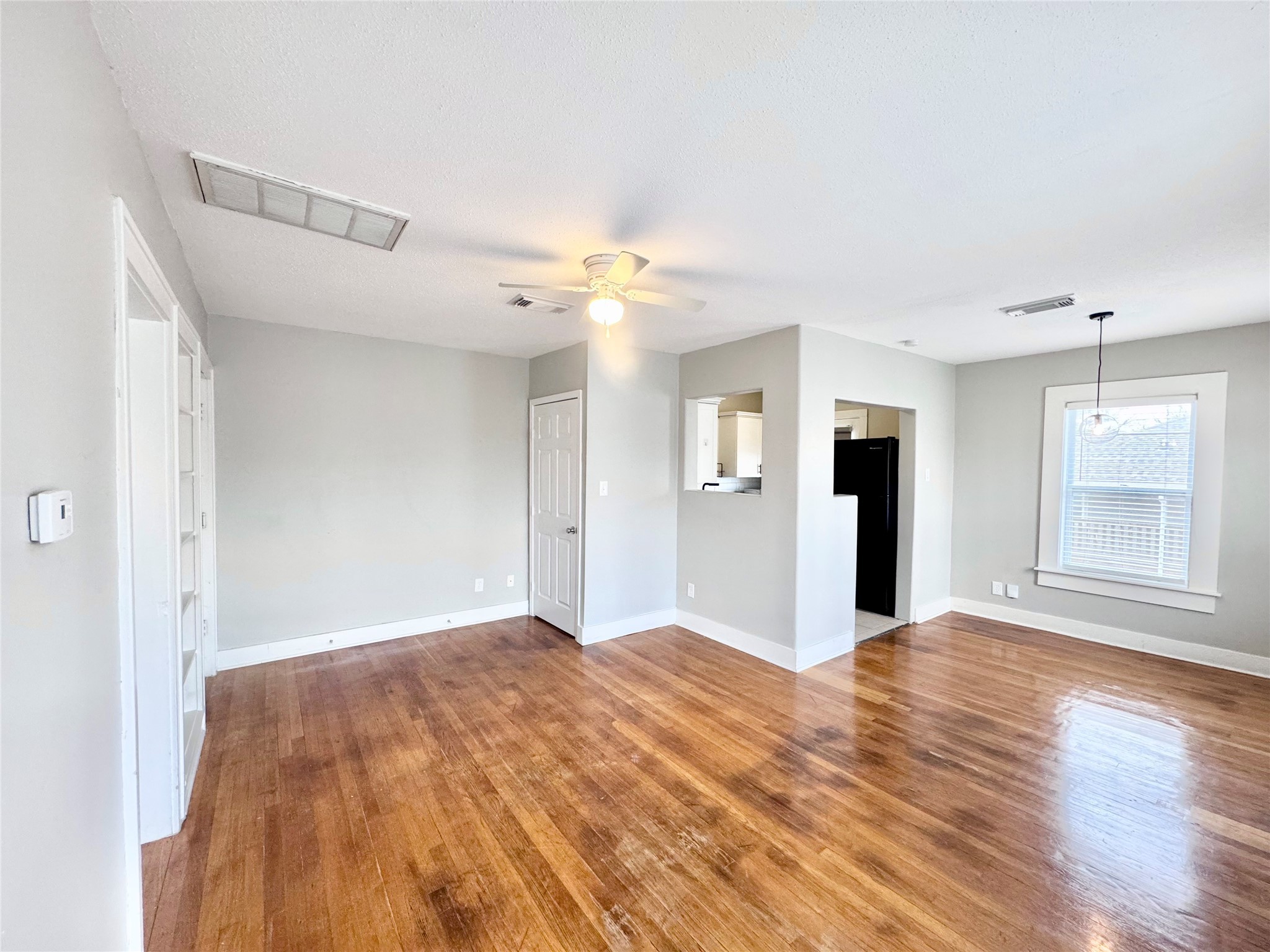 a view of an empty room with window and a kitchen