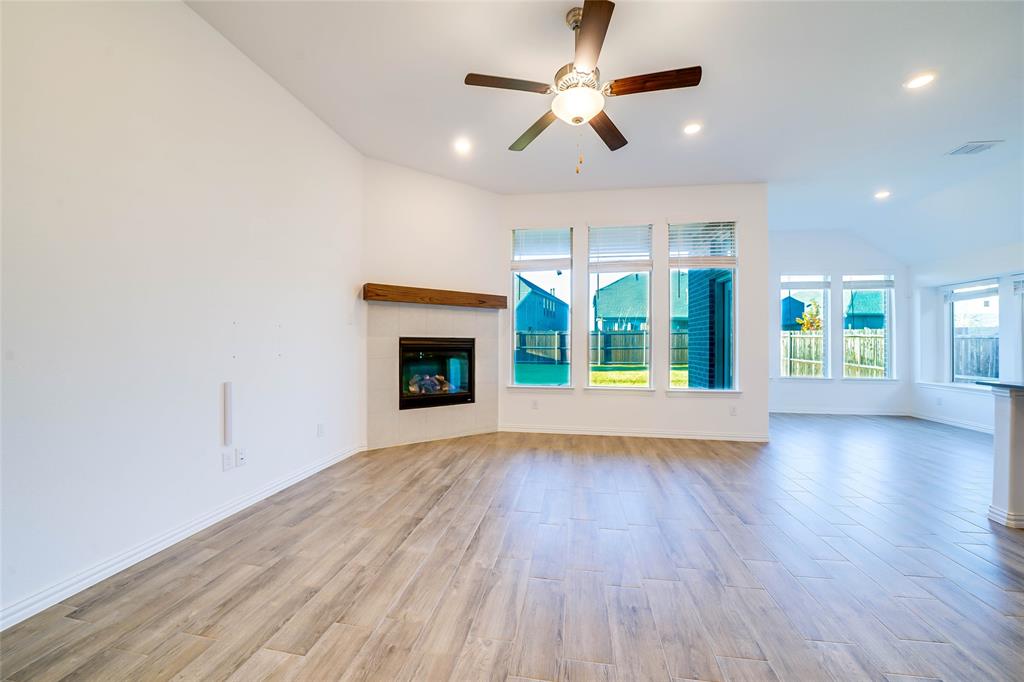 3420 Prairie Place McKinney, TX 75071 - Photo 5 of 37 an empty room with large windows a fireplace a ceiling fan and wooden floor
