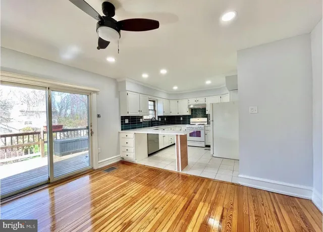 a kitchen with stainless steel appliances kitchen island granite countertop a refrigerator a sink a stove and white cabinets with wooden floor