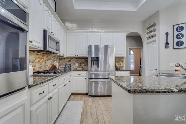 a kitchen with granite countertop a sink stainless steel appliances and white cabinets