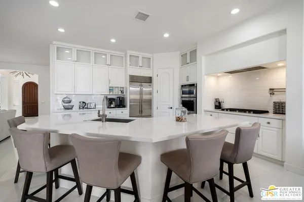a kitchen with stainless steel appliances kitchen island granite countertop a dining table chairs and a refrigerator