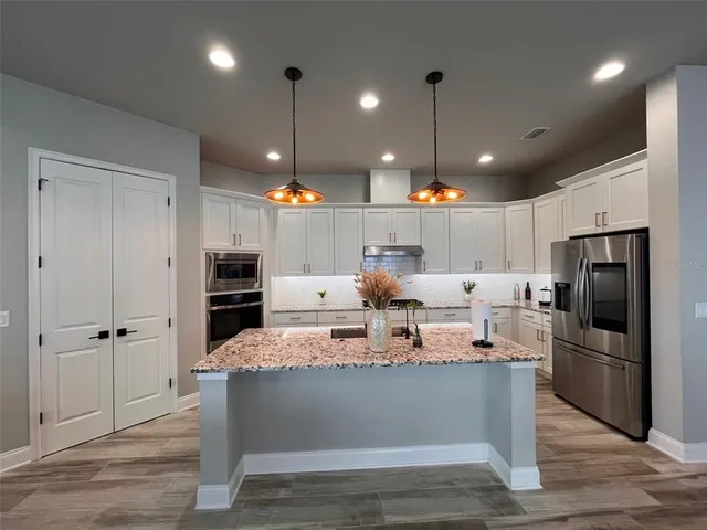 a large kitchen with stainless steel appliances kitchen island granite countertop a refrigerator a oven and a wooden floor