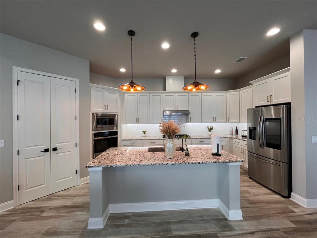 12149 Southwest 33rd Place Gainesville, FL 32608 - Photo 4 of 35 a large kitchen with stainless steel appliances kitchen island granite countertop a refrigerator a oven and a wooden floor