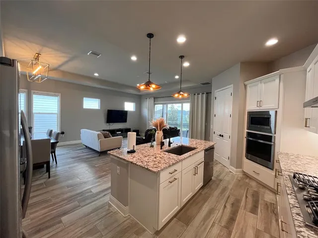 a large white kitchen with stainless steel appliances kitchen island a stove a refrigerator a oven and a dining table with wooden floor