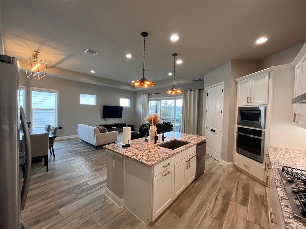 12149 Southwest 33rd Place Gainesville, FL 32608 - Photo 5 of 35 a large white kitchen with stainless steel appliances kitchen island a stove a refrigerator a oven and a dining table with wooden floor
