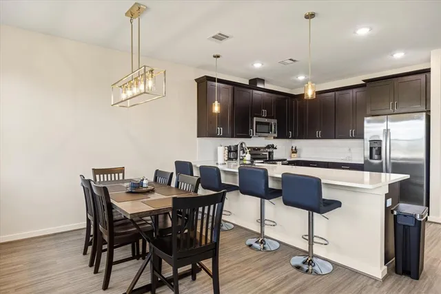 a kitchen with stainless steel appliances kitchen island granite countertop a dining table chairs refrigerator and microwave