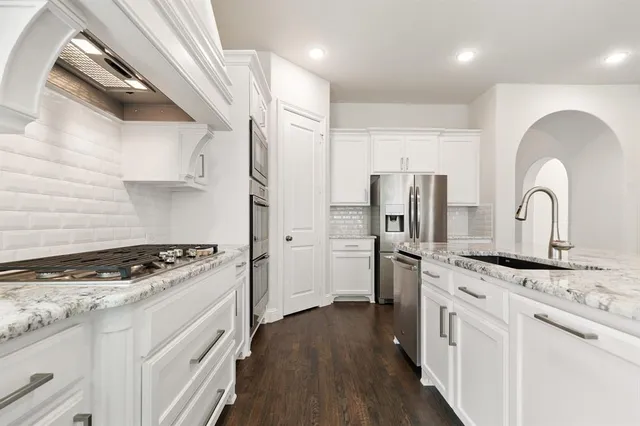 a kitchen with stainless steel appliances granite countertop a stove a sink dishwasher a refrigerator and white cabinets with wooden floor