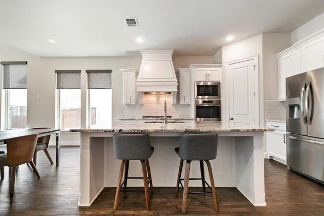 a kitchen with stainless steel appliances granite countertop a stove a refrigerator a sink a stove and white cabinets with wooden floor