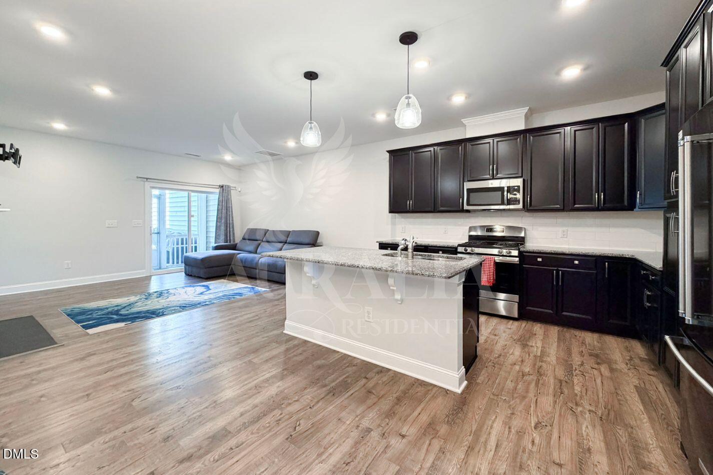 1306 Farm Pond Trail Durham, NC 27703 - Photo 11 of 46 a large kitchen with stainless steel appliances kitchen island granite countertop a stove top oven a sink and a living room with wooden floor