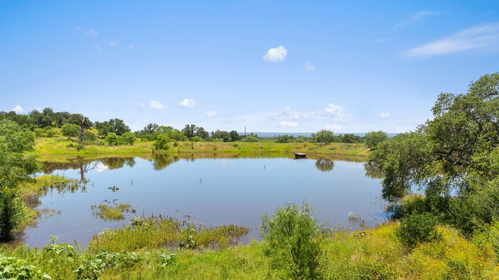 1101 Crider Road Marble Falls, TX 78654 - Photo 3 of 37 A tranquil pond reflecting a clear sky, surrounded by vibrant greenery and distant hills.