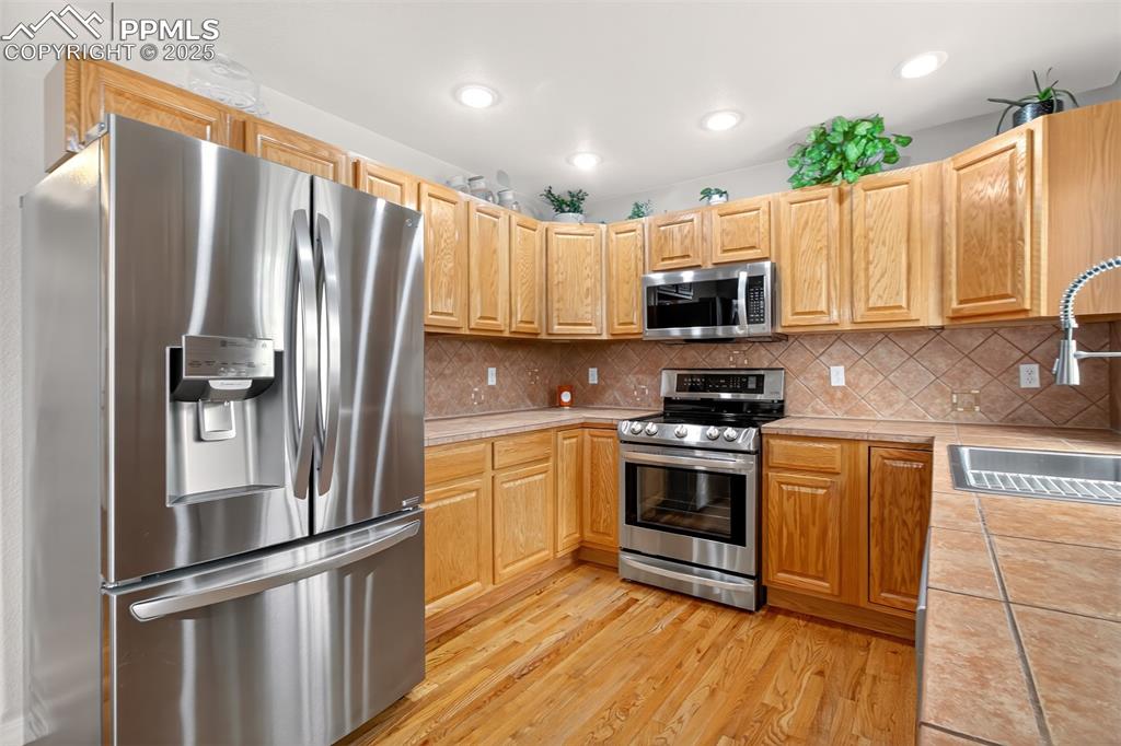 7374 Maybeck View Peyton, CO 80831 - Photo 6 of 38 a kitchen with kitchen island granite countertop a refrigerator oven a sink and dishwasher with wooden floor