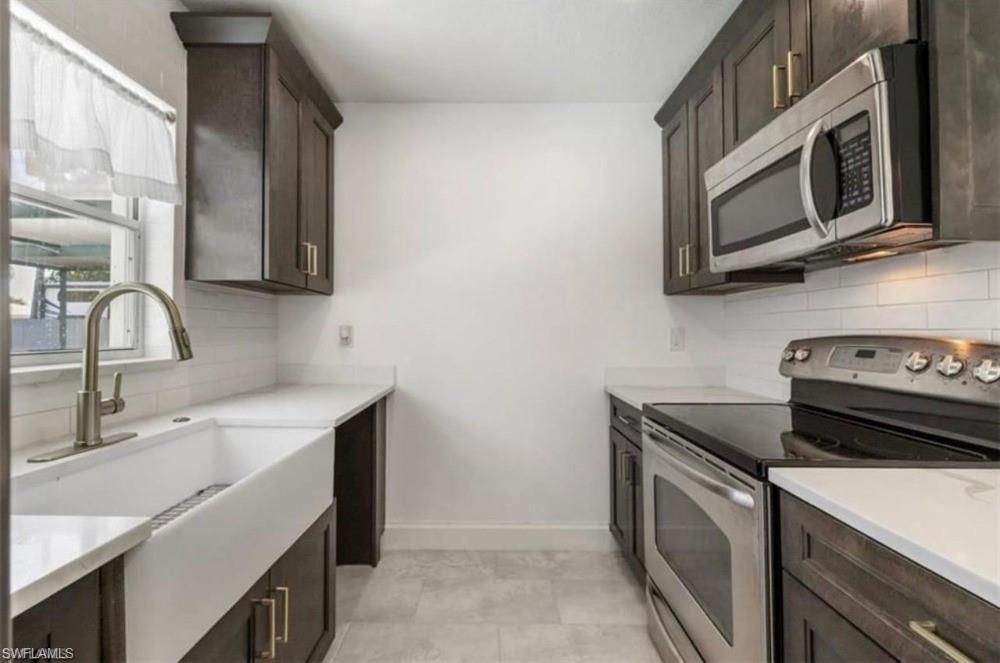 1948 46th Street Southwest Naples, FL 34116 - Photo 6 of 14 Galley kitchen featuring dark wood-finish cabinetry, white countertops, a white farmhouse sink with a brushed nickel faucet, and stainless steel appliances including a range and microwave