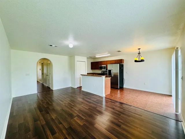an empty room with wooden floor kitchen view and a window