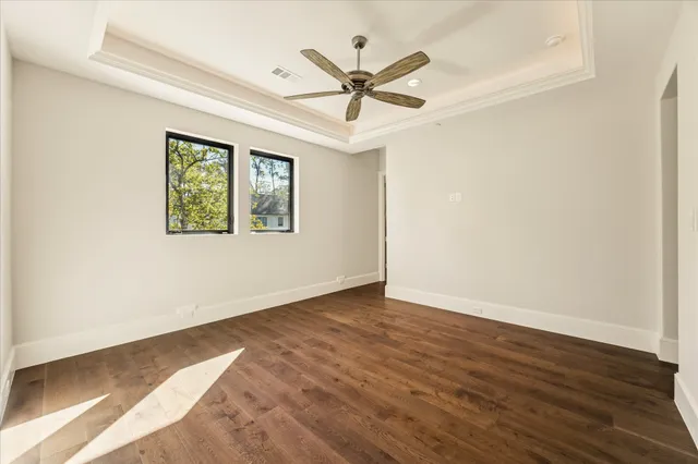 an empty room with wooden floor ceiling fan and windows