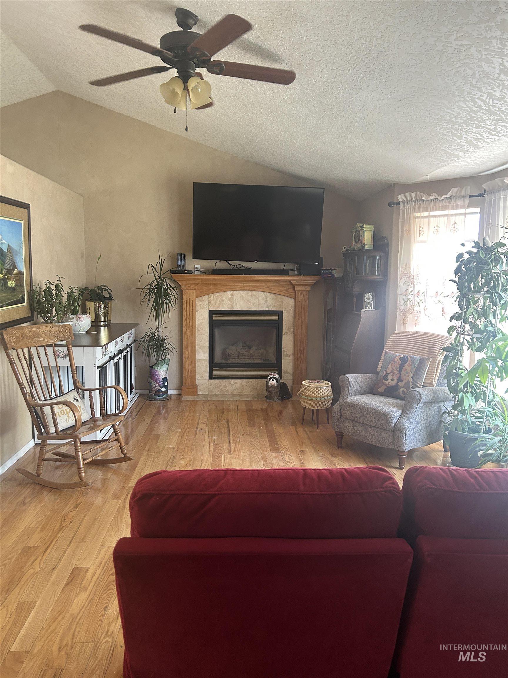 1444 East Doberman Street Meridian, ID 83642 - Photo 15 of 31 Living space featuring vaulted ceilings, wood-finish flooring, a ceiling fan with integrated lighting, and a fireplace with a stone surround and wood mantel