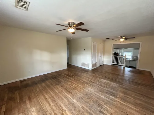 an empty room with wooden floor chandelier fan and windows