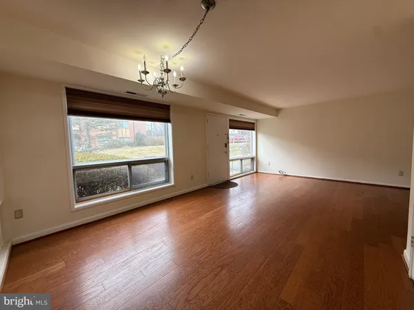 an empty room with wooden floor chandelier and windows