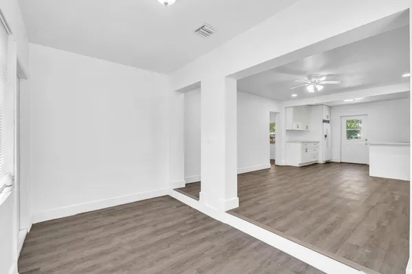 an empty room with wooden floor and kitchen view