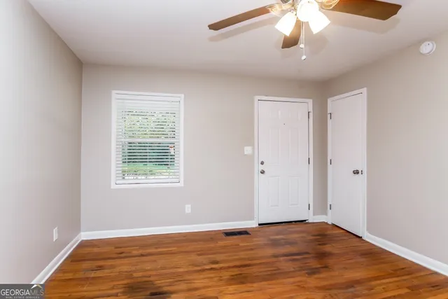 an empty room with wooden floor chandelier fan and windows