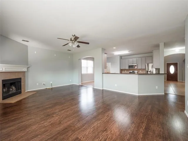 a view of an empty room with wooden floor and a kitchen