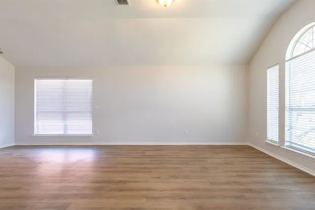 an empty room with wooden floor and windows with curtains