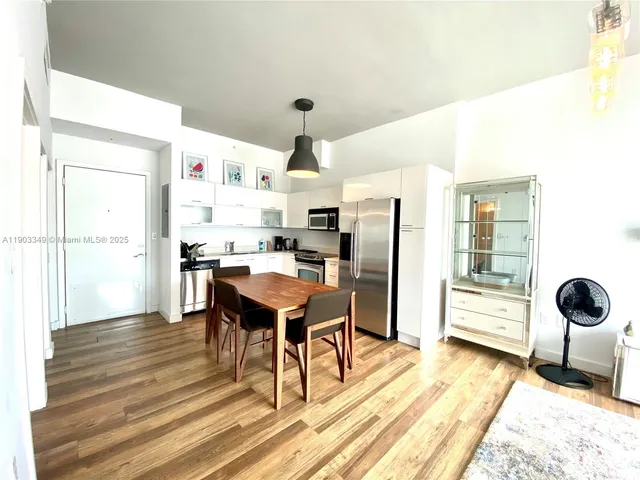 a kitchen with stainless steel appliances a stove a refrigerator and a dining table with wooden floor