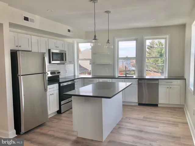 a kitchen with granite countertop a refrigerator a sink a stove and oven with wooden floor