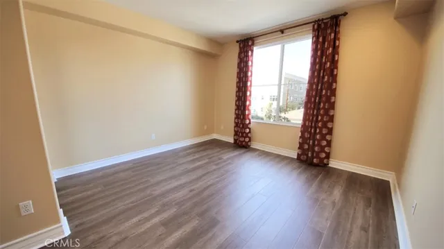 an empty room with wooden floor and windows with curtains
