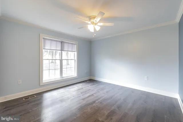 an empty room with wooden floor chandelier fan and windows