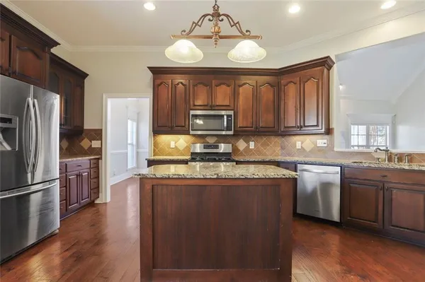 a kitchen with stainless steel appliances granite countertop a refrigerator a stove top oven a sink and dishwasher with wooden floor