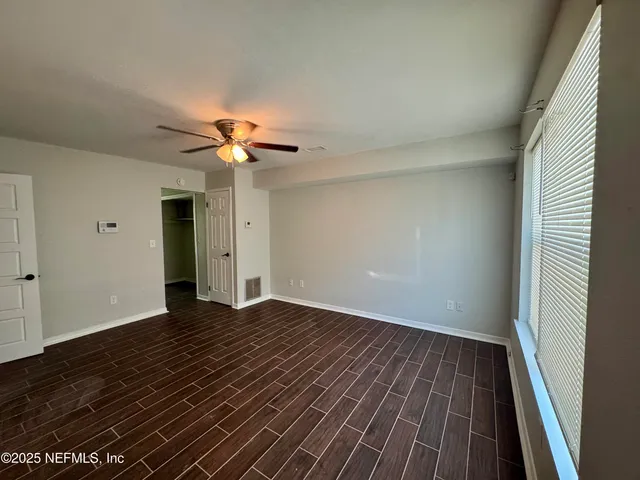 a view of an empty room with wooden floor and a ceiling fan