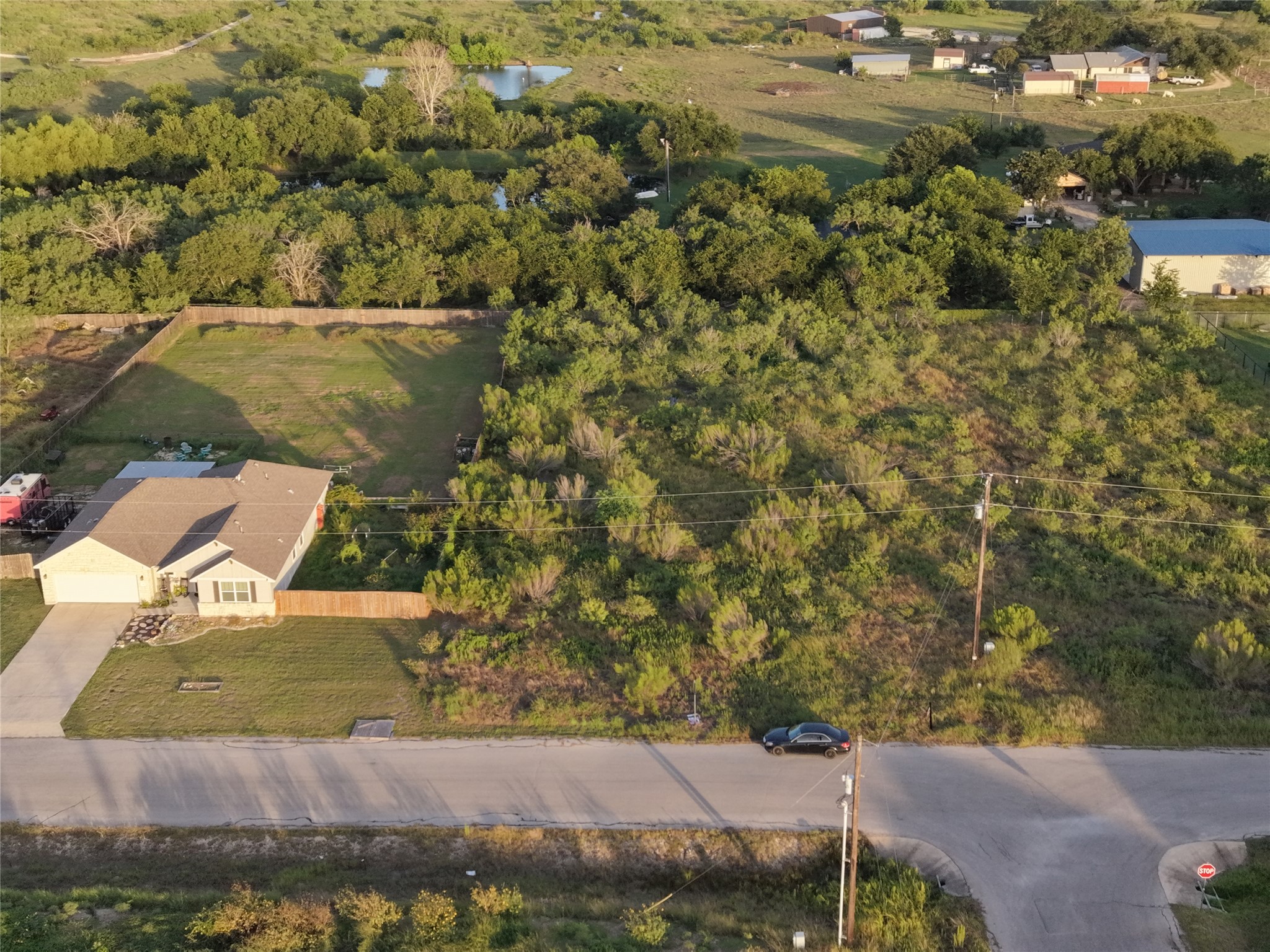 232 East Ridge Lane Kyle, TX 78640 - Photo 27 of 36 An aerial perspective reveals a charming single-story residence nestled in a verdant landscape, showcasing a private yard, long driveway, and nearby pond.