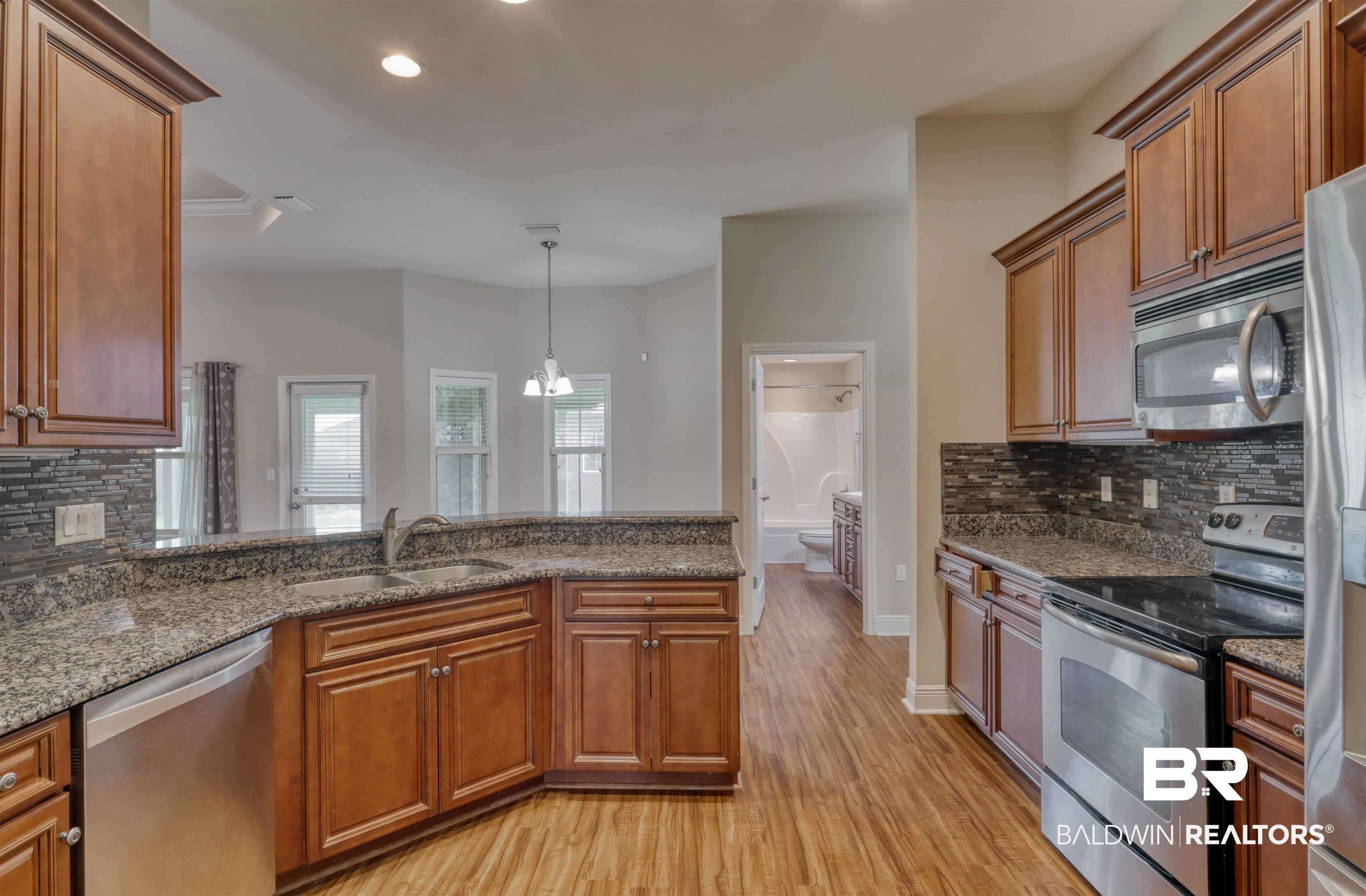 14794 Troon Drive Foley, AL 36535 - Photo 11 of 33 Kitchen with appliances with stainless steel finishes, a sink, light wood finished floors, brown cabinetry, and tasteful backsplash