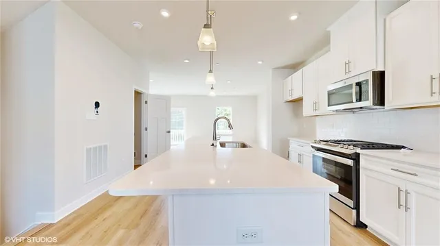 a kitchen with stainless steel appliances a stove a sink a microwave a refrigerator and white cabinets