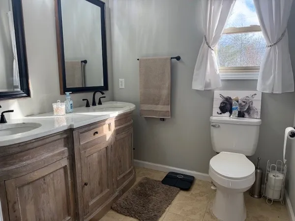 a bathroom with a toilet a sink a mirror a window and vanity