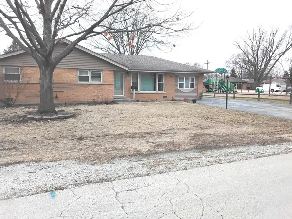 a front view of a house with a dirt yard and a large tree