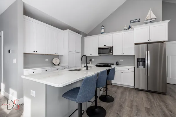 a kitchen with stainless steel appliances a sink a stove a refrigerator cabinets and chairs